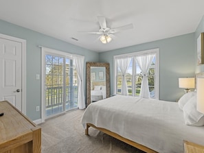 A bedroom with a bed, a ceiling fan, and a view of the outdoors through large windows.