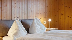 A hotel room with a wooden panel wall, a bed with white linens, and a bedside table with a lamp. - Apartment 'Wegscheiderhof' with Mountain View, Private Terrace and Wi-Fi (Dobbiaco)