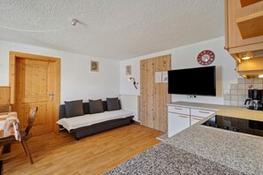 A compact living space with a sofa, a television, a wooden door, and a kitchen area. - Apartment 'Wegscheiderhof' with Mountain View, Private Terrace and Wi-Fi (Dobbiaco)