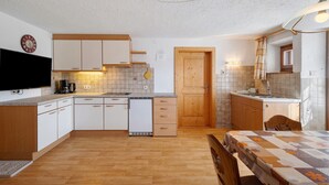 A compact kitchen with white cabinets, a wooden door, a built-in dishwasher, and a flat-screen TV. - Apartment 'Wegscheiderhof' with Mountain View, Private Terrace and Wi-Fi (Dobbiaco)