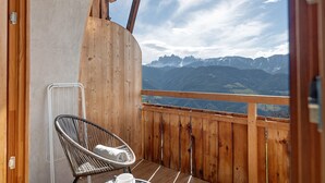 Un balcon en bois avec une chaise et une table, donnant sur un paysage montagneux.
