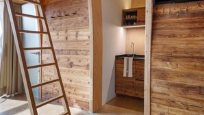 Un interior de madera con una escalera, una cocina con pileta y armarios, y un ventanal con cortinas.