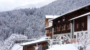 Una cabaña de madera con balcón, rodeada de árboles y montañas nevadas.