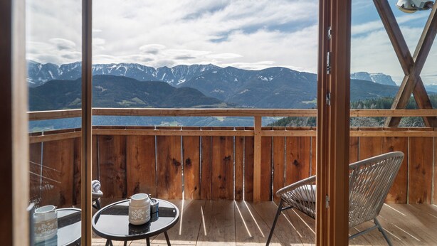 Una terraza de madera con una mesa y sillas, y vistas a montañas nevadas. Cuenta con una barandilla de madera.