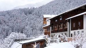 A wooden chalet with a balcony, surrounded by snow-covered trees and mountains. - Studio 'Pavilion Water' with Mountain View, Shared Terrace and Wi-Fi (Velturno)
