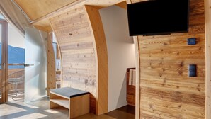 A modern room with wooden walls, a flat-screen TV, a bench, and a door leading to a balcony. - Studio 'Pavilion Water' with Mountain View, Shared Terrace and Wi-Fi (Velturno)