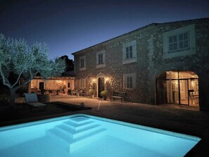 Un edificio de piedra con piscina, zona de estar al aire libre y un árbol.