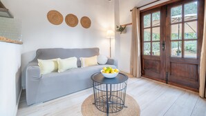 Ein Wohnzimmer mit einem grauen Sofa, einem runden schwarzen Tisch mit Obstschale, einer Lampe und einer Holztür mit Blick.