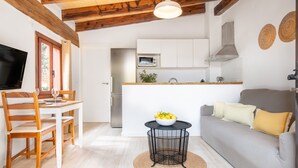 Eine moderne Küche mit weißen Schränken, einer Mikrowelle und einem Spülbecken. Es gibt einen Essbereich mit Tisch und Stühlen, sowie eine Couch mit Kissen.