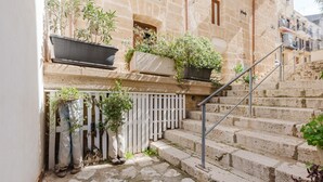 A stone building with a staircase, potted plants, and a white fence.