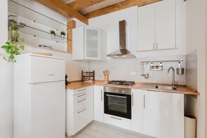 Una cucina moderna con mobili bianchi, forno integrato, cappa aspirante in acciaio inox e piano di lavoro in legno.
