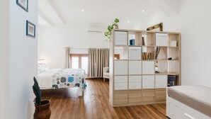 A bedroom with a wooden floor, a bed with a patterned bedspread, a white wardrobe, and a potted plant.