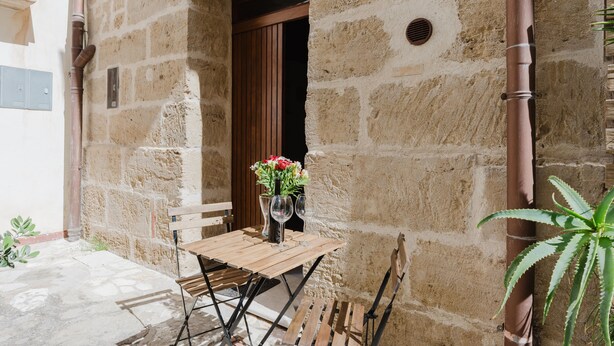 Un bâtiment en pierre avec une table et des chaises en bois, un vase rempli de fleurs et une plante en pot.