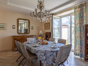 A dining room with a chandelier, a table set for four, and a view of the outdoors through large windows.
