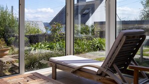 Un invernadero con una butaca de madera, ventanas amplias y vistas a una zona residencial.