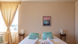 Habitación de hotel con cama, dos mesitas de noche, una ventana con cortinas, un cartel en la pared y vistas al exterior.