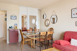 A dining area with a glass table and chairs, a red sofa, and a wall with mirrors and a framed picture.