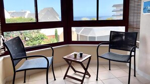 Ein Balkon mit zwei Stühlen und einem kleinen Tisch, große Fenster mit Blick auf Gebäude und Grünflächen.