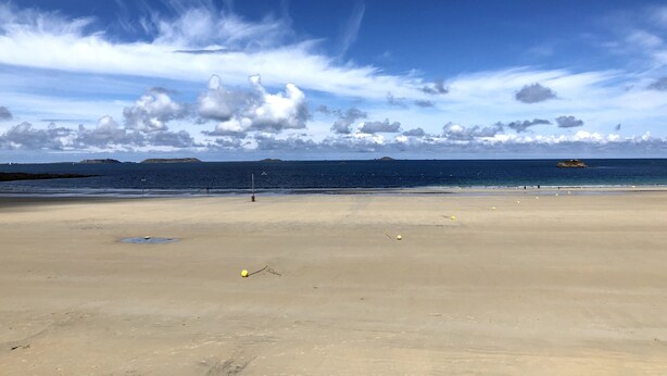 Ein Strand mit blauem Himmel, ruhiger See und fernen Landformen.