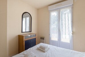 Un dormitorio con cama, cómoda, espejo y una puerta con cortinas de encaje.