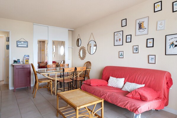 Una sala de estar amoblada con un sofá rojo, una mesa de comedor con sillas y una zona de cocina con un refrigerador y un armario.