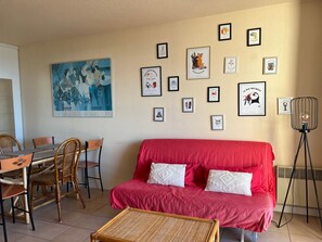 Un salon avec un canapé rouge, une table à manger entourée de chaises et divers tableaux encadrés accrochés au mur.