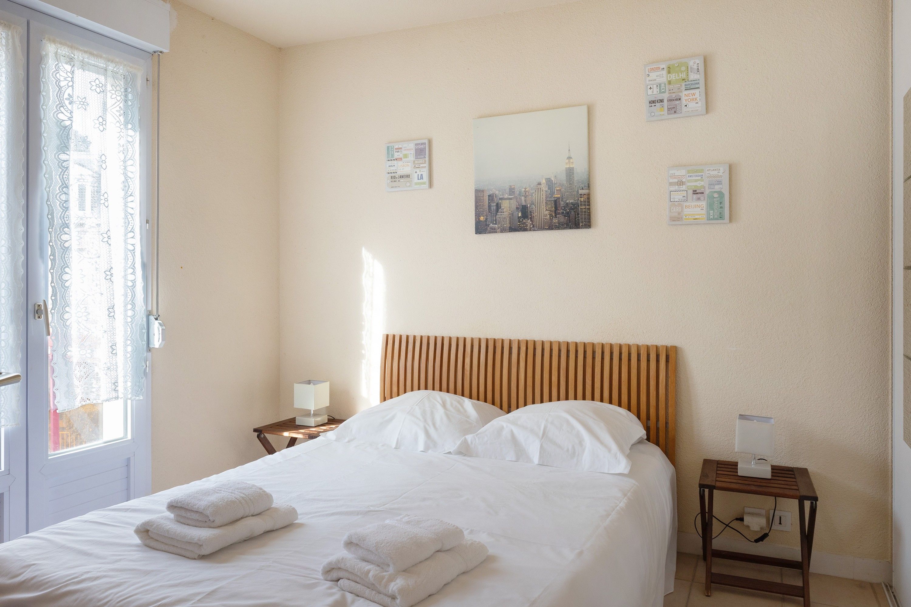 A hotel room with a bed, a nightstand, a lamp, and a wall with travel-themed decorations.