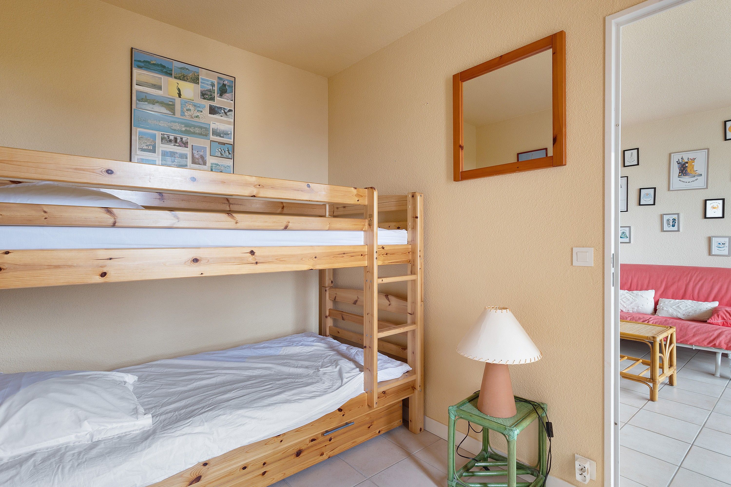 Ein Schlafraum mit Etagenbett, Holzrahmen, einem kleinen Hocker mit Lampe und einer Wand mit gerahmten Bildern.