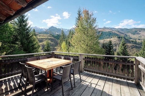 A wooden deck with a table and chairs, overlooking a mountainous landscape.