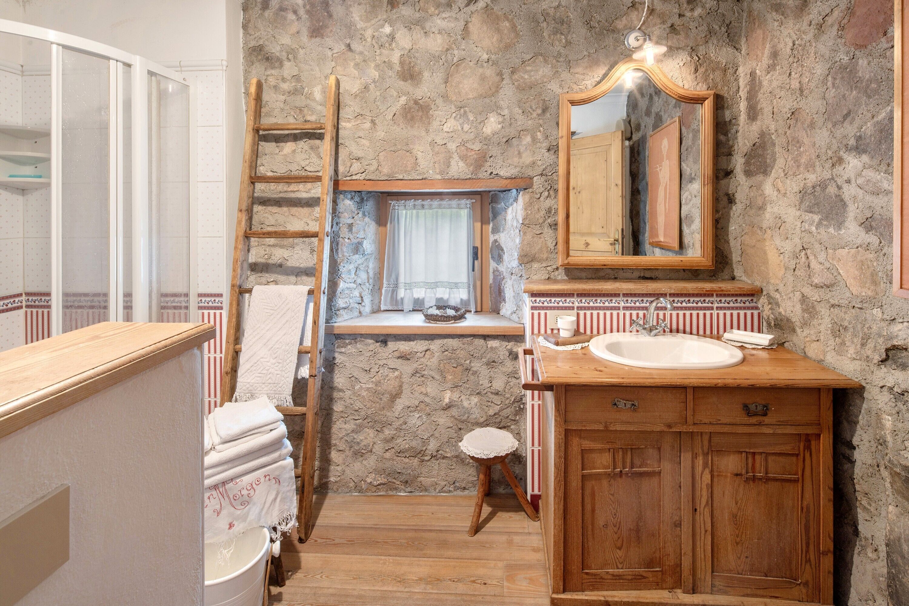 A bathroom with a stone wall, wooden vanity, a mirror, and a window with a curtain.