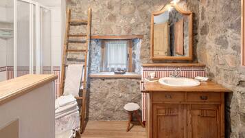 A bathroom with a stone wall, wooden vanity, a mirror, and a window with a curtain.