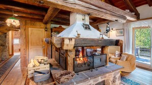 Un interior rústic amb una llar de pedra, bigues de fusta i una zona d'estades acollidora.