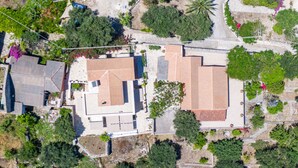 An aerial view of a residential area with multiple houses, some with sloped roofs, surrounded by greenery and trees.