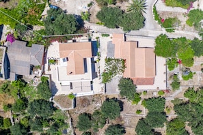 Vista aérea de una zona residencial con varias casas, algunas con techos inclinados, rodeada de vegetación y árboles.