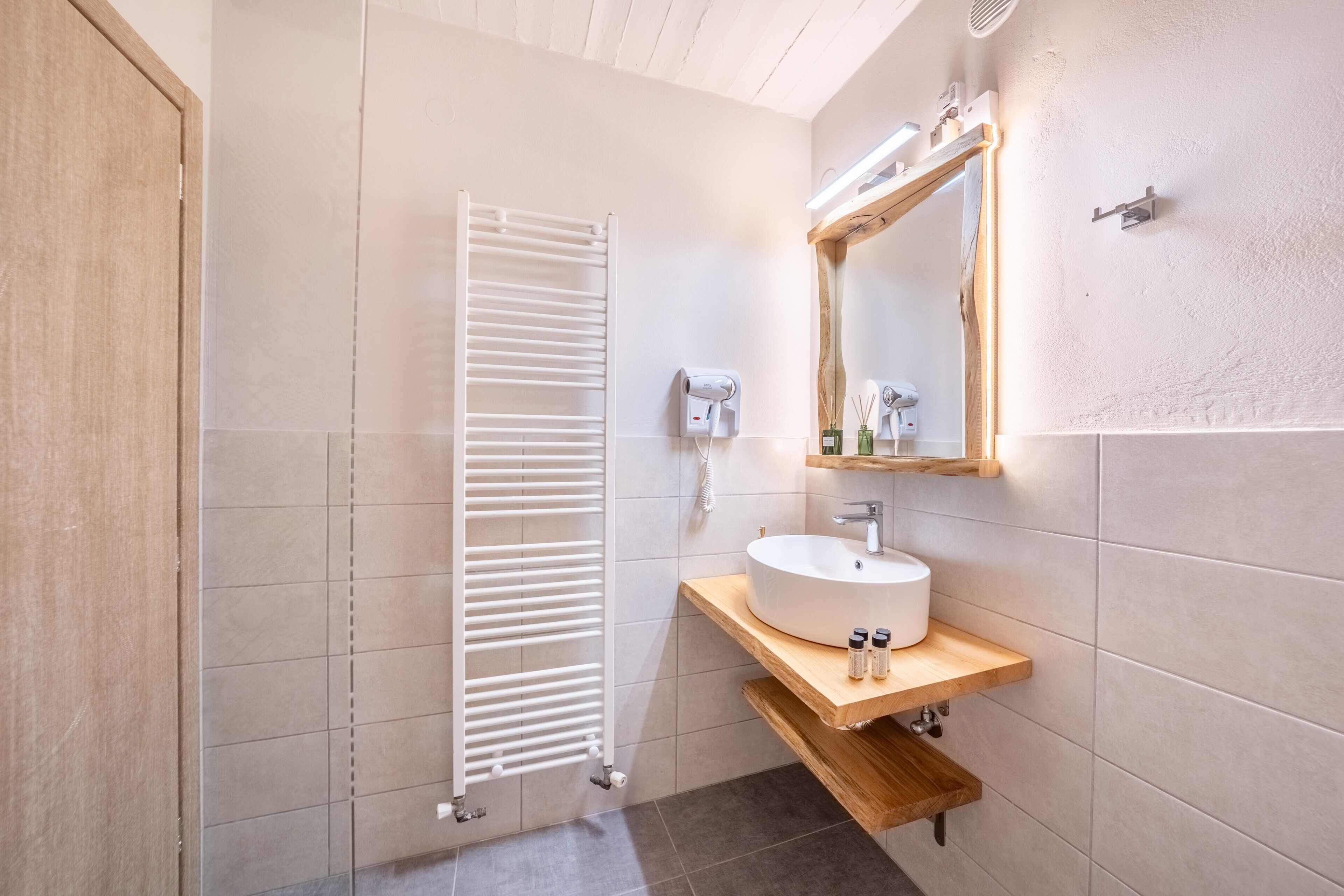 Un baño moderno con un lavamanos blanco, tocador de madera, barra para toallas y un espejo con marco de madera.