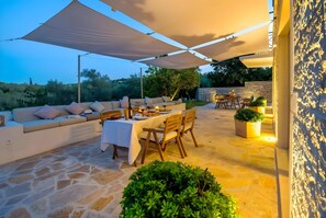 An outdoor patio with stone flooring, a sofa, dining table, and chairs, shaded by large white canopies.