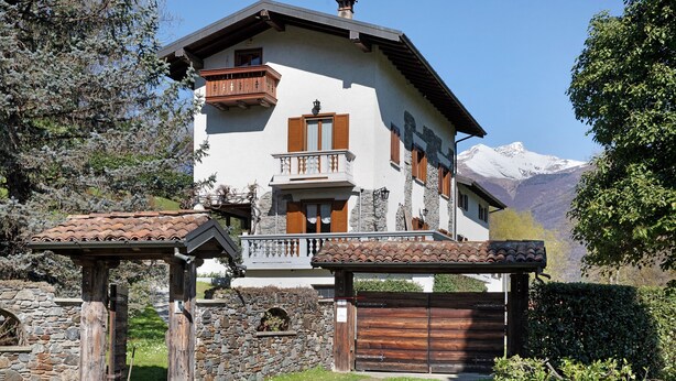 A chalet with a balcony, stone wall, and a view of snow-capped mountains. - Apartment 'Casa Letizia' with Private Pool, Private Terrace and Wi-Fi (Colico)