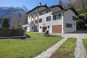 A two-story house with a stone facade, a wooden deck, and a view of a mountain.