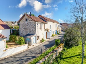 A stone building with a tiled roof, a narrow street, and a stone wall with greenery. - Gîte La Grange – Comfort and Relaxation in the Heart of Périgord Vert (Saint-Martial-d'Albarède)