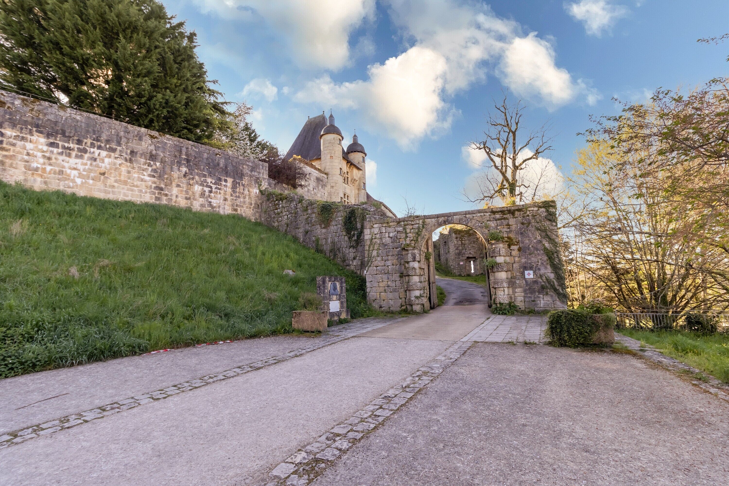 Un bâtiment historique en pierre, doté d’une grande entrée en arc de cercle, d’une colline verdoyante et d’un ciel dégagé.