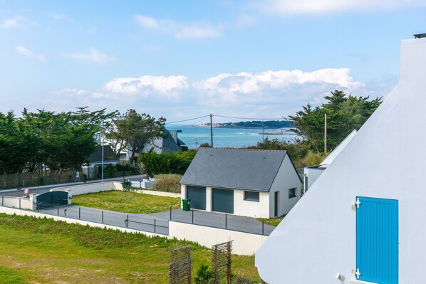 A coastal residential area with a white building featuring a blue door, a paved pathway, and a view of the sea.