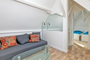 A modern living room with a glass coffee table, grey sofa, colorful cushions, and a large mirror.