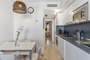 A modern kitchen with stainless steel appliances, a dining area with a white table and chairs, and a hallway leading to another room. - Apartment 'Beach Escape' with Sea View, Wi-Fi and Air Conditioning (Benalmádena)