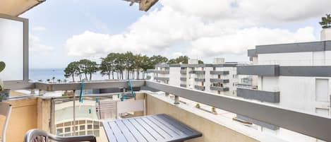 A balcony with a table and chairs, overlooking a residential area with multiple buildings and a clear sky.