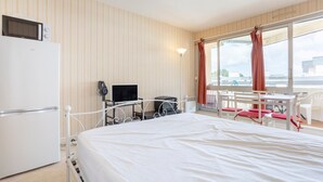 A hotel room with a bed, a desk with a computer, a TV, a refrigerator, and a window with curtains. - Studio Apartment 'Vue Mer - 50m De La Plage' with Sea View, Private Terrace and Wi-Fi (Bénodet)