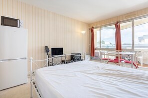 A hotel room with a bed, a desk with a computer, a TV, a refrigerator, and a window with curtains.