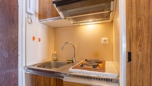 A compact kitchenette with a stainless steel sink, a built-in stove, and wooden cabinetry. - Studio Apartment 'Vue Mer - 50m De La Plage' with Sea View, Private Terrace and Wi-Fi (Bénodet)