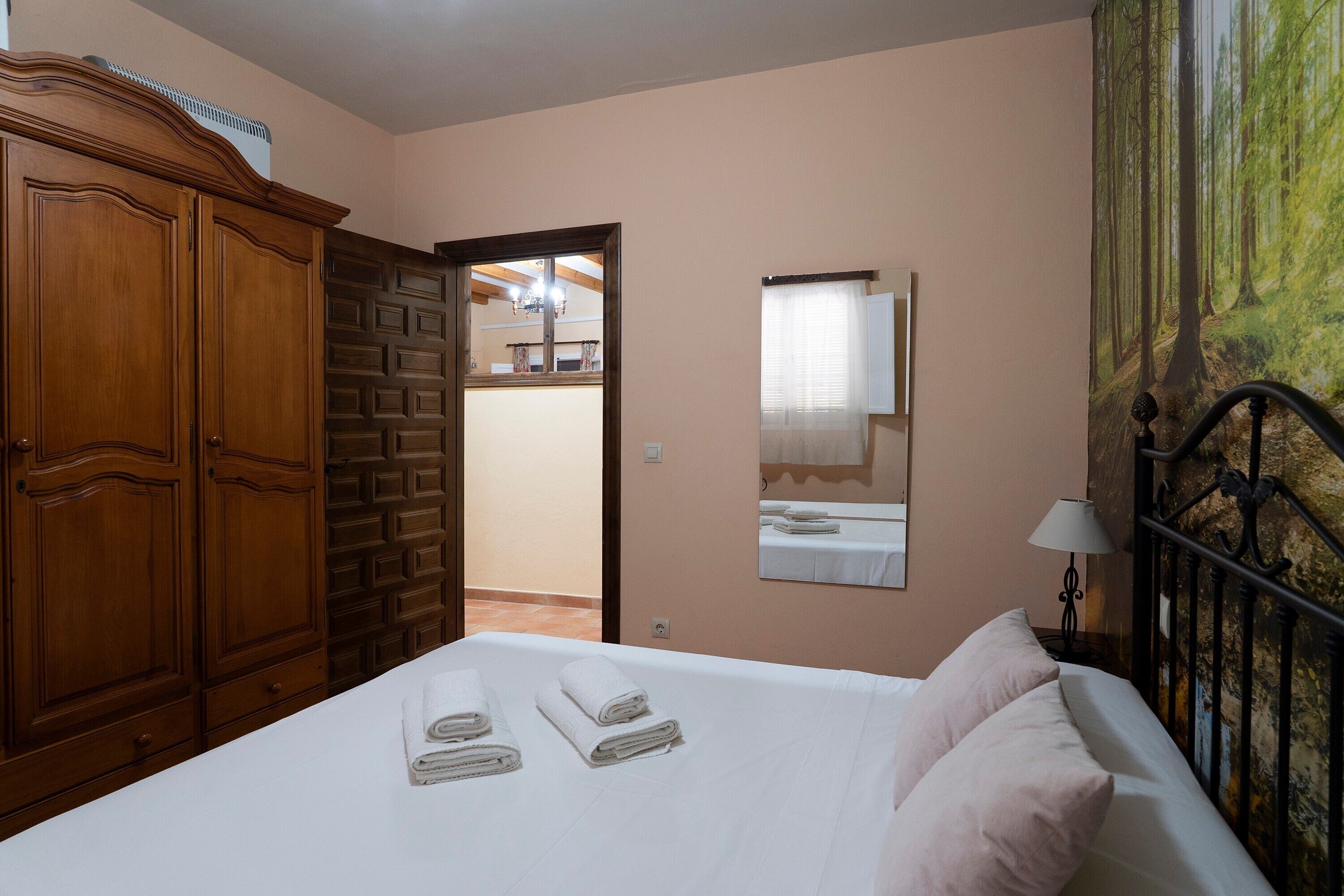 Een slaapkamer met een bed, een kledingkast, een spiegel en een deur die naar een andere kamer leidt.