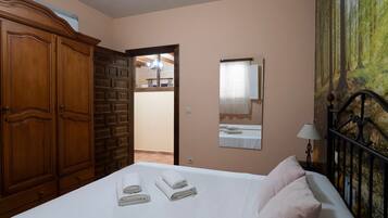 Een slaapkamer met een bed, een kledingkast, een spiegel en een deur die naar een andere kamer leidt.