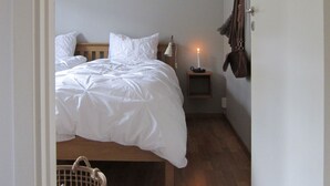 A bedroom with a bed, a bedside table with a candle, and a coat hanging on the wall. - Vargen 2 by Interhome (Tännäskröket)